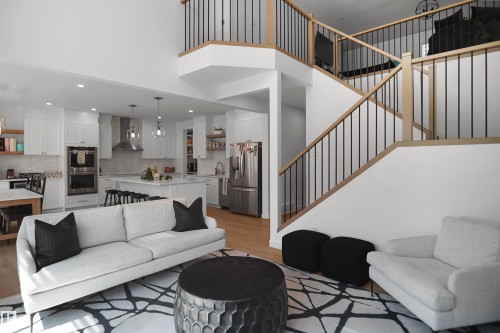 Open-concept living space featuring wood-finish flooring and a multi-level staircase with natural wood handrails and black metal spindles - 5802 Soleil Boulevard, Beaumont, AB 