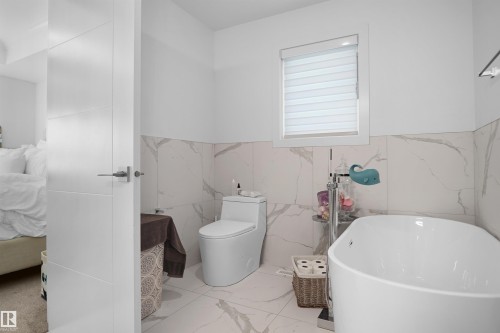 Bathroom with marble-look wall and floor tile, featuring a freestanding soaking tub, a contemporary toilet, and a window with horizontal blinds - 5802 Soleil Boulevard, Beaumont, AB 
