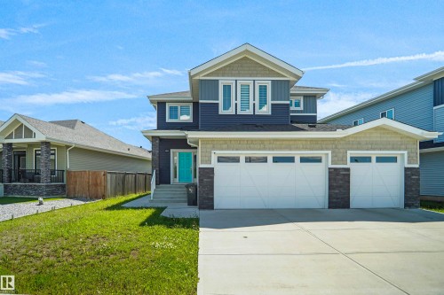 Contemporary two-story residence featuring a striking blue and tan exterior with stone accents, a prominent teal entry door, a two-car garage, and a concrete driveway - 5802 Soleil Boulevard, Beaumont, AB 