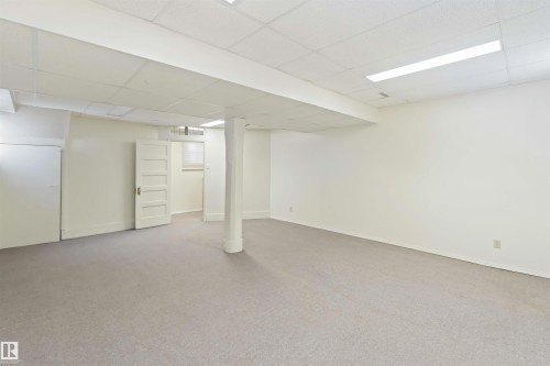 Spacious room featuring light-toned carpeting, white walls, and a suspended acoustic tile ceiling - 13156 101 St Nw, Edmonton, AB 