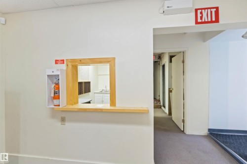 Interior corridor featuring a service window with a wood-finish frame and counter, white walls, and carpet flooring - 13156 101 St Nw, Edmonton, AB 