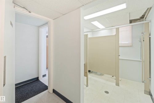 Commercial restroom featuring privacy partitions, tile flooring, and integrated lighting - 13156 101 St Nw, Edmonton, AB 
