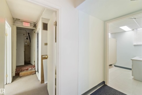 Hallway with carpet flooring leading to a utility space with exposed piping and an illuminated exit sign - 13156 101 St Nw, Edmonton, AB 