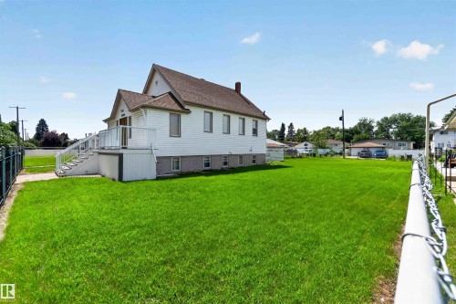 Expansive green lawn surrounds a white-sided residence featuring a multi-tiered deck with white railings - 13156 101 St Nw, Edmonton, AB 