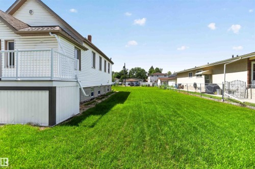 Extensive grassy yard featuring a white-sided exterior, a white deck with railings, and a partial view of a neighboring property - 13156 101 St Nw, Edmonton, AB 