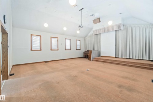 Spacious room featuring vaulted ceilings with pendant and recessed lighting, multiple windows with blinds, an elevated platform, and full-wall drapes - 13156 101 St Nw, Edmonton, AB 