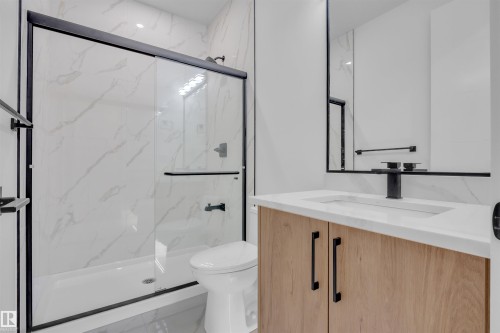 Modern bathroom featuring a walk-in shower with black-framed glass doors and white marble-look paneling - 3604 44 Avenue, Beaumont, AB - Indoor Photo Showing Bathroom