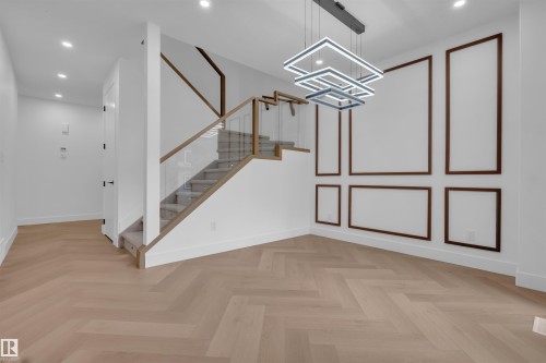 Herringbone wood-finish flooring complements the contemporary staircase with glass railing and wood handrail - 3604 44 Avenue, Beaumont, AB - Indoor Photo Showing Other Room