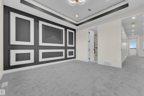 Accent wall with black and white molding detail, tray ceiling with contrasting trim, recessed lighting, light gray carpeting, and an adjacent hallway with additional recessed lighting - 3604 44 Avenue, Beaumont, AB - Indoor Photo Showing Other Room