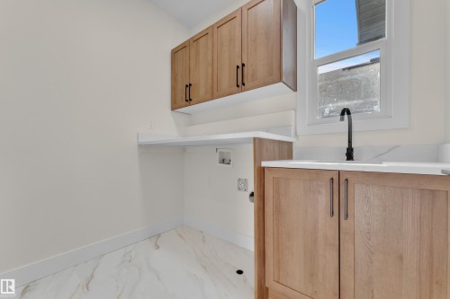 Laundry area featuring white walls, wood-finish cabinetry with dark hardware, a white countertop with integrated sink, and a black gooseneck faucet - 3604 44 Avenue, Beaumont, AB - Indoor