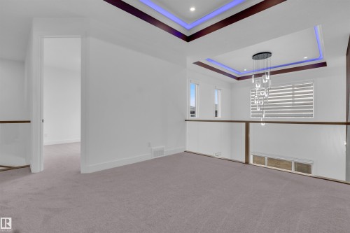 Upper-level open space featuring carpet flooring, a contemporary chandelier, two windows, and a glass-paneled railing system with wood-finish top rails - 3604 44 Avenue, Beaumont, AB - Indoor Photo Showing Other Room
