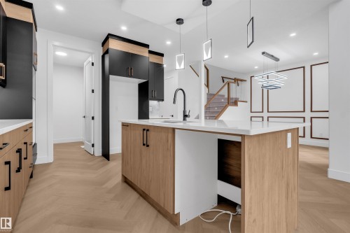 Kitchen featuring a central island with a white countertop and undermount sink, wood-finish cabinetry with black hardware, and pendant lighting - 3604 44 Avenue, Beaumont, AB - Indoor Photo Showing Kitchen With Upgraded Kitchen