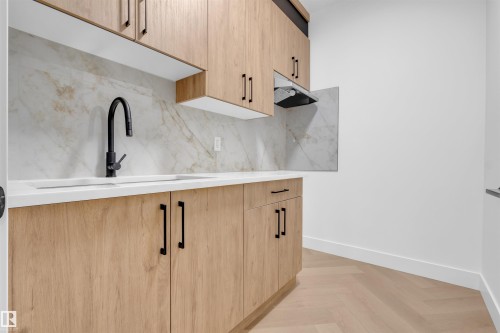Kitchenette featuring wood-finish cabinetry with black hardware, white countertop, and a full-height marble-style backsplash - 3604 44 Avenue, Beaumont, AB - Indoor