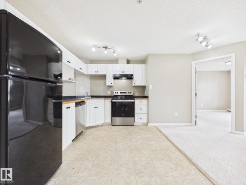 Kitchen featuring white cabinetry, dark countertops, a black refrigerator, a stainless steel dishwasher, and a black range with an overhead microwave - #309 5350 199 St Nw, Edmonton, AB 