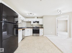 Kitchen featuring white cabinetry, dark countertops, a black refrigerator, a stainless steel dishwasher, and a black range with an overhead microwave - 