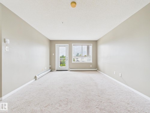 Spacious room featuring neutral carpeting, light-toned walls, and a white trim finish - #309 5350 199 St Nw, Edmonton, AB 