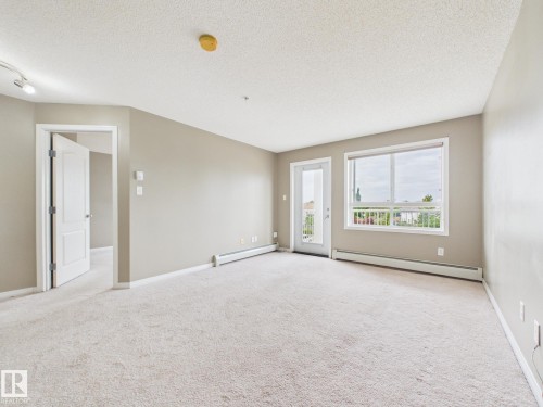 Spacious living area featuring light-toned carpeting, neutral wall paint, and a textured ceiling - #309 5350 199 St Nw, Edmonton, AB 