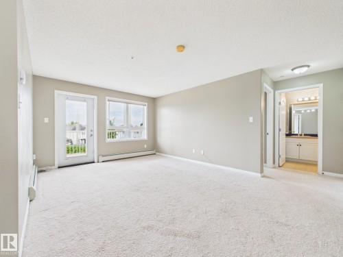 Bright living area featuring light-toned carpeting and neutral wall colors - #309 5350 199 St Nw, Edmonton, AB 