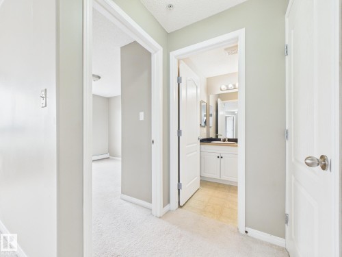 Hallway featuring light neutral wall paint and white baseboards - #309 5350 199 St Nw, Edmonton, AB 