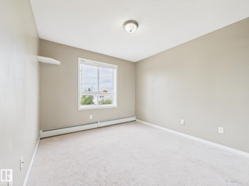Neutral-toned room with light-colored carpeting and a window featuring white trim - #309 5350 199 St Nw, Edmonton, AB 