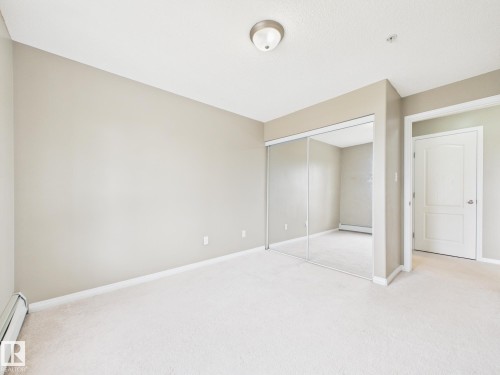 Neutral-toned room featuring a soft carpet, mirrored closet doors, a white interior door, and a flush-mount ceiling light - #309 5350 199 St Nw, Edmonton, AB 