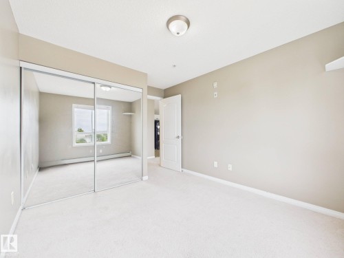 Spacious room featuring mirrored closet doors, neutral wall paint, and white trim - #309 5350 199 St Nw, Edmonton, AB 