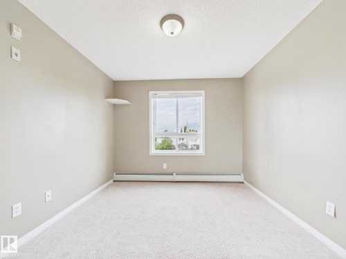 Neutral-toned interior featuring carpet flooring, a single window, baseboard heating, and a flush-mount ceiling light - #309 5350 199 St Nw, Edmonton, AB 