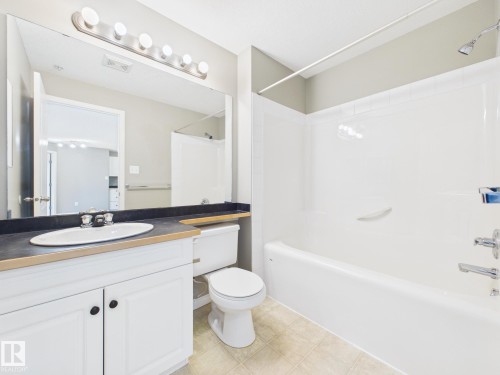 Full bathroom featuring a white vanity with dark countertop, an oval undermount sink, and a large mirror with vanity lighting - #309 5350 199 St Nw, Edmonton, AB 