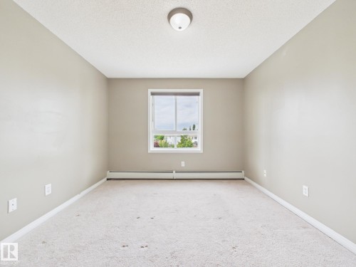 Neutral-toned room with a single window, overhead lighting fixture, and baseboard heating - #309 5350 199 St Nw, Edmonton, AB 