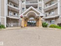 Building exterior featuring a covered entrance with stone-clad pillars, glass double doors, and multiple balconies with white railings - #309 5350 199 St Nw, Edmonton, AB 