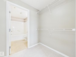 Carpeted closet with wire shelving and a doorway opening to a bathroom featuring a white bathtub, toilet, and tile flooring - 
