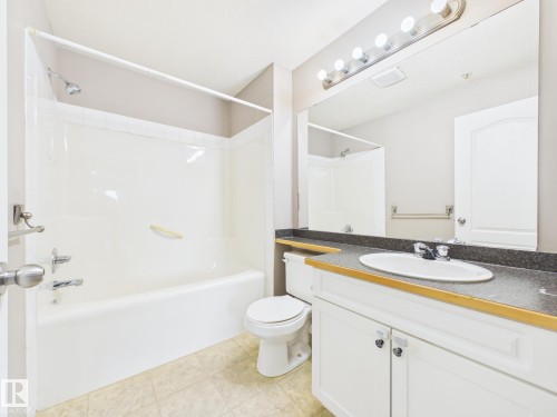 Bathroom featuring a white vanity with a dark countertop, an integrated sink, and a large mirror - #309 5350 199 St Nw, Edmonton, AB 