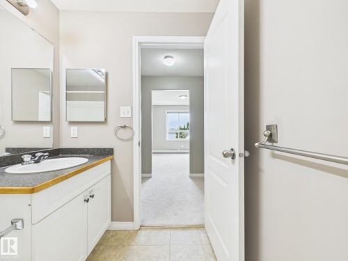 Bathroom vanity featuring white cabinetry, a dark countertop, and a built-in sink with chrome fixtures - #309 5350 199 St Nw, Edmonton, AB 