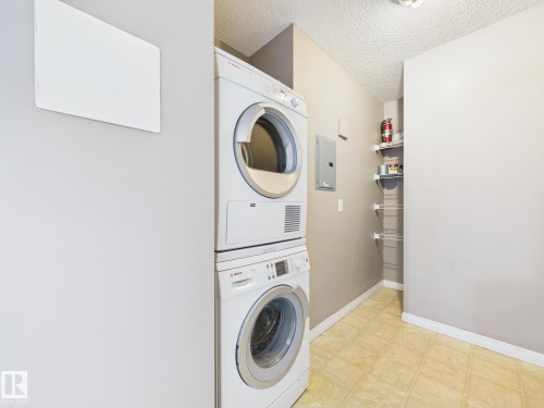 Dedicated laundry area with stacked appliances, checkered tile flooring, and neutral wall tones - #309 5350 199 St Nw, Edmonton, AB 