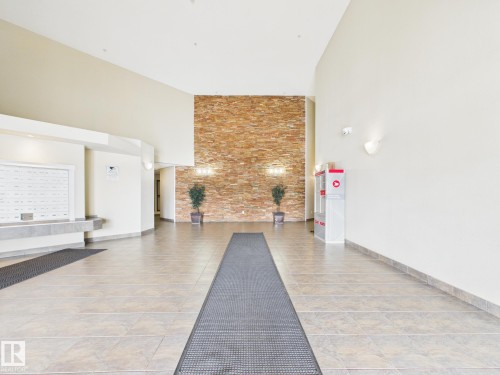 Spacious entryway featuring a stacked stone accent wall and tile flooring - #309 5350 199 St Nw, Edmonton, AB 