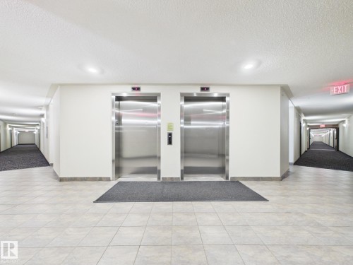 Dual stainless steel elevators framed by neutral walls and light-toned tile flooring - #309 5350 199 St Nw, Edmonton, AB 