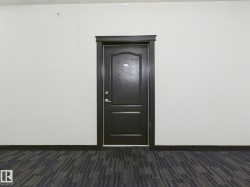 Richly toned door with decorative paneling and polished chrome hardware, framed by dark trim, set against light neutral walls and patterned carpet flooring - 