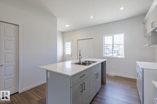 Kitchen featuring a central island with a double basin sink, light grey cabinetry, white countertops, and wood-finish flooring - 3619 Triomphe Boulevard, Beaumont, AB - Indoor Photo Showing Kitchen With Double Sink