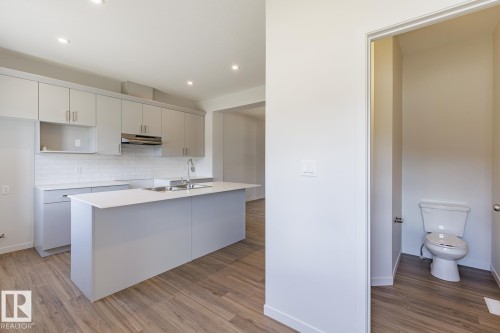 Modern kitchen featuring light gray cabinetry, a central island, stainless steel appliances, a subway tile backsplash, and wood-finish flooring - 3619 Triomphe Boulevard, Beaumont, AB - Indoor