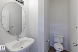 Modern powder room featuring a wall-mounted sink with chrome faucet, an oval frameless mirror, and wood-finish flooring - 