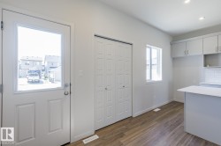 Entry door with upper glass panel, wood-finish flooring, white bi-fold closet doors, light gray cabinetry, and a white subway tile backsplash - 