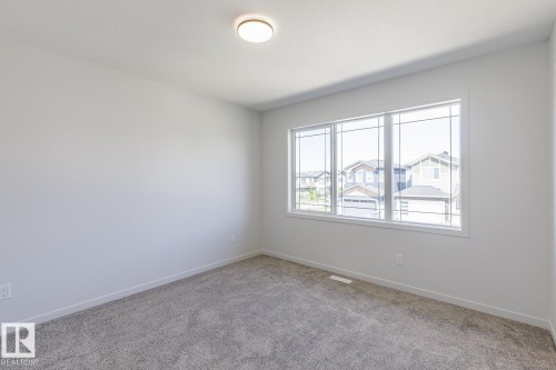 Bright room featuring a large multi-pane window, neutral gray carpeting, white baseboards, and a flush-mount ceiling light - 3619 Triomphe Boulevard, Beaumont, AB - Indoor Photo Showing Other Room