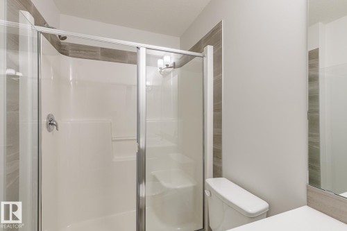 Bathroom featuring a glass-enclosed shower with a built-in seat, chrome fixtures, and a white shower surround - 3619 Triomphe Boulevard, Beaumont, AB - Indoor Photo Showing Bathroom