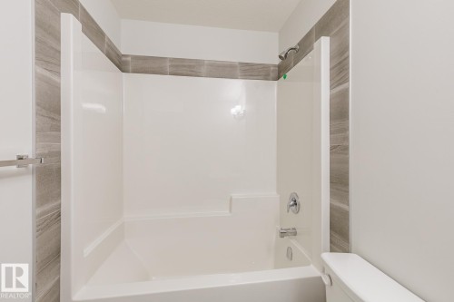 White bathtub and shower combination unit featuring a chrome shower head and faucet - 3619 Triomphe Boulevard, Beaumont, AB - Indoor Photo Showing Bathroom