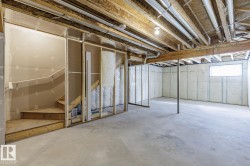 Unfinished basement featuring exposed wood joists, concrete flooring, and framed walls - 