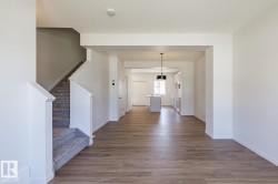 Open-concept living area featuring wood-finish flooring, a carpeted staircase with white balusters, white baseboards, and a modern black ceiling light fixture - 