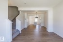 Open-concept living area featuring wood-finish flooring, a carpeted staircase with white balusters, white baseboards, and a modern black ceiling light fixture - 3619 Triomphe Boulevard, Beaumont, AB  - Indoor Photo Showing Other Room 