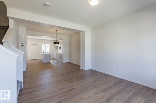 Open-concept layout featuring wood-finish flooring, white walls, and a contemporary kitchen island with a sink - 3619 Triomphe Boulevard, Beaumont, AB - Indoor Photo Showing Other Room