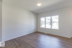 Spacious room featuring wood-finish flooring, white baseboards, and a large multi-pane window - 