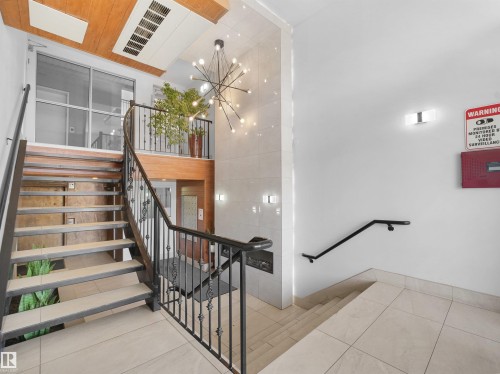 Multi-level interior featuring a contemporary chandelier, wrought iron railings, and wood-finish ceiling accents - #207 10606 102 Av Nw, Edmonton, AB 
